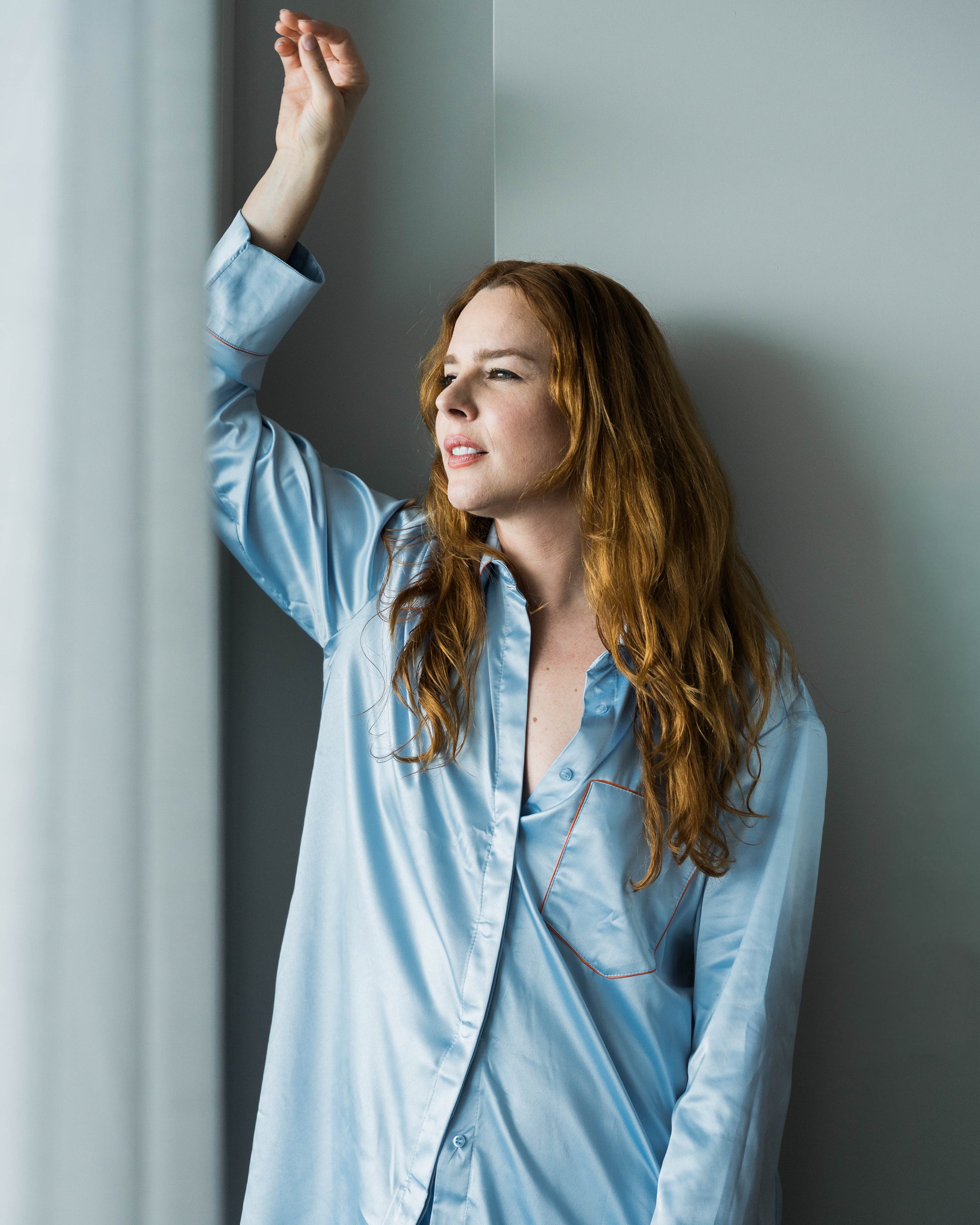 Woman in light blue pajama set standing against a gray wall.